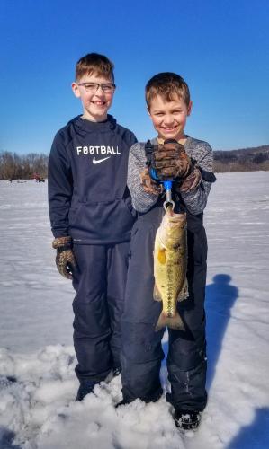 Two young boys on iced lake hold a bass