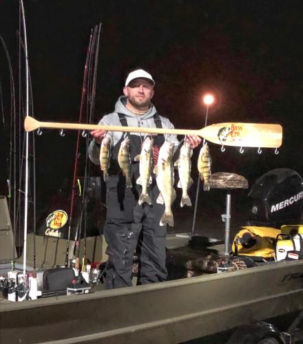Walleye angler staning in a boat at night with six walleye catches