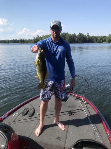 Bass fisher standing on a bass boat holding a large bass