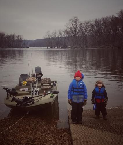 Two you boys standing on shore next to a fishing boat