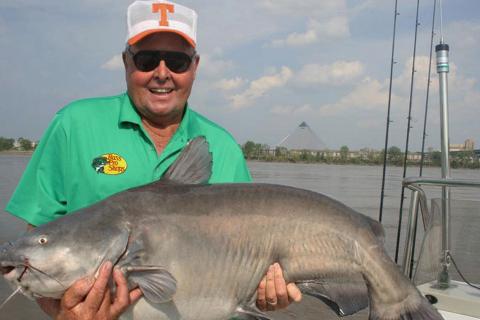 Bill Dance standing on a boat with a large blue catfish