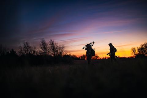 Two hunters walking through a field at sunset