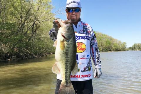 Major League Fishing Pro James Watson standingon a boat with a largemouth bass