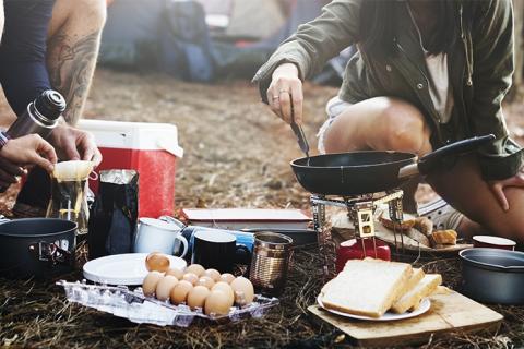 Two campers preparing breakfast food at a campsite over a fire