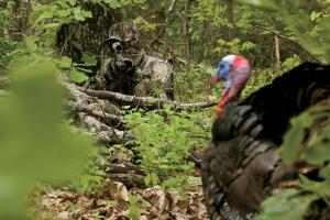 Turkey hunting leaning next to a tree preparing to shoot a gobbler