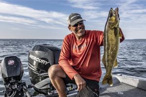 Anger sitting in a fishing boat holding up a large walleye fish