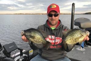 Angler sitting in a boat holding two large black Crappie in each hand 