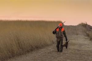 Pheasant hunter walking down a prairie road with pheasant in hand