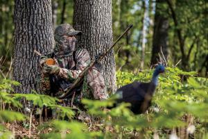 Turkey hunter leaning up to a tree using a turkey friction call