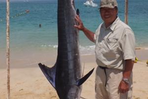 Striped Marlin hanging from a rope next to angler on Baja beach 