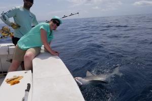 Lady angler stretching over the side of the boat posing with the shark she caught