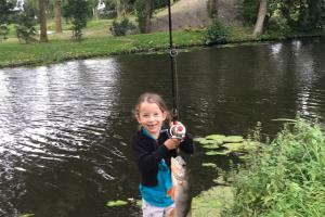 Small girl wih rod and reel at  edge of pond hold up her fish