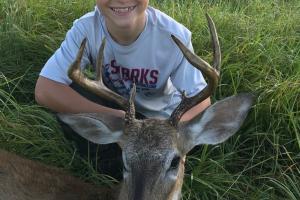 Young boy deer hunter sitting near his buck harvest