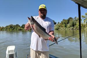 Salmon angler standing on the boat holding up a large salmon he caught