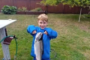 Young boy standing in his yard holding a 6lbs pink salmon that is almost as big as he is