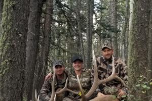 3 hunters in the woods posing next to a harvested bull elk