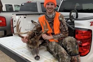 Deer hunter is sitting in back of truck with his harvested buck