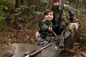 Deer hunter posing with deer and young son
