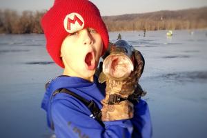 Young ice angler holding an open mouthed fish with his mouth open too