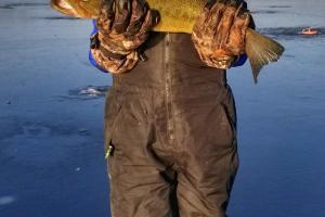 Boy standing on frozen lake hold up the fish he caught ice fishing