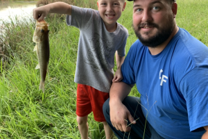 Young boy standing at the edge of a pond hold bass