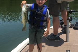 Boy angler on bass boat holding largemouth bass