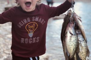 Toddler at waters edge holding up a stringer of crappie