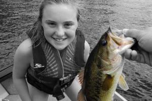 Girl on a boat poasing next to a largemouth bass