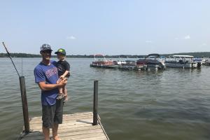 Young angler wearing a Bass Pro hat with father on a dock