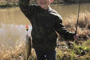 Young boy fishing a lake holding small bass