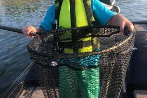 Boy angler hold his netted fish standing in a boat