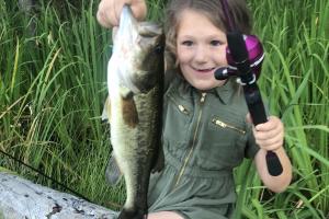 Young girl sitting on a log holding up a large bass