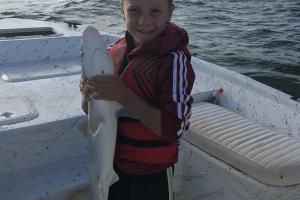 Young boy standing in a boat holding a small shark 