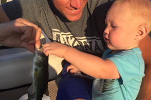 Young toddler reaching for a small bass his father is holding