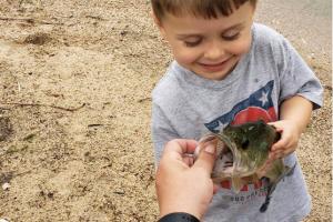 Small angler holding a bass looking into its mouth