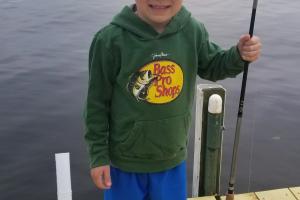 Young boy on a dock wearing a Bass Pro shirt hold a rod & reel combo