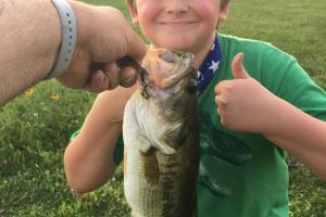 Young boy angler giving thumbs up with bass at hand