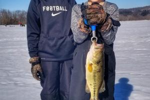 Two young boys on iced lake hold a bass