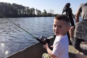 Boy sitting on a cooler in a boat fishing 