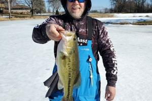 Bass angler standing in the snow holding a large bass