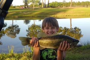 Boy angler pond fishing & holding a bass