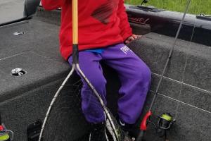 Young angler sitting in a boat with a fishing net full of fish