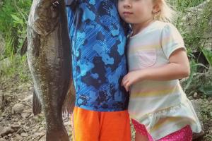 Two young children hold up a bass
