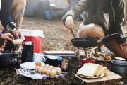 Two campers preparing breakfast food at a campsite over a fire